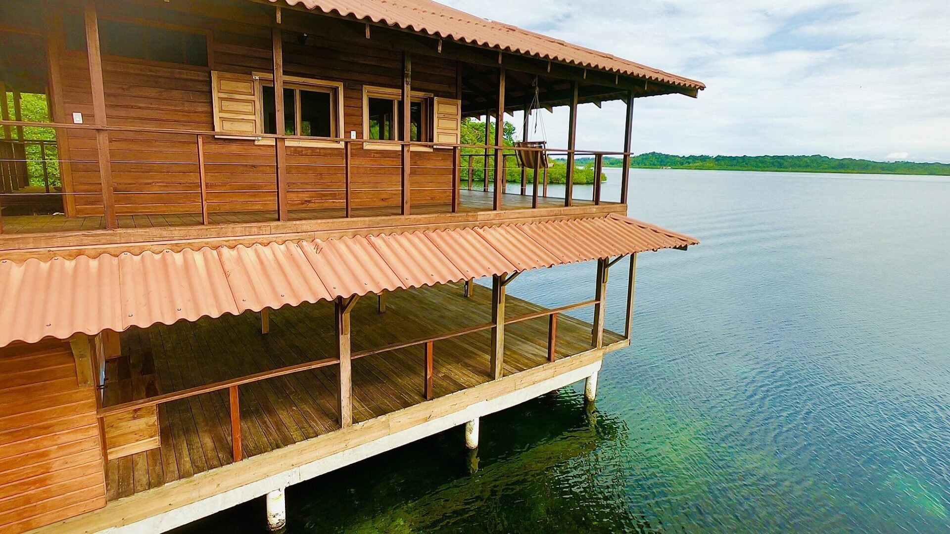 A wooden house on the water with a deck.