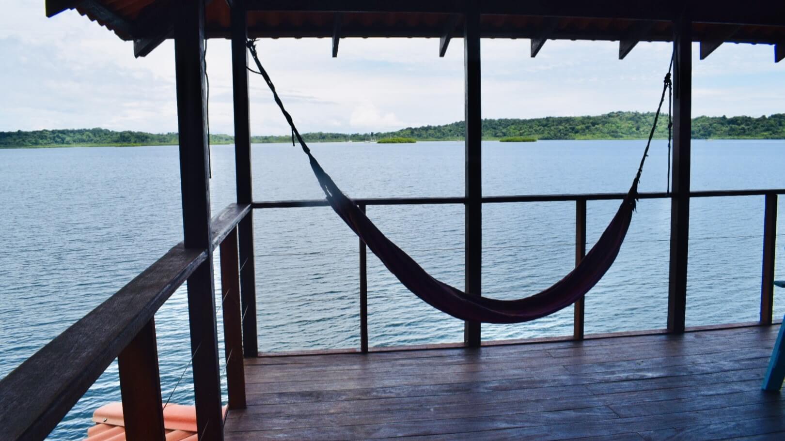 A hammock hanging from the side of a wooden deck.
