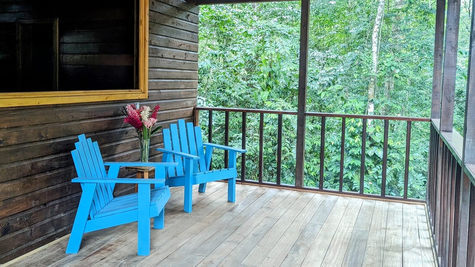 A porch with two blue chairs and a table.