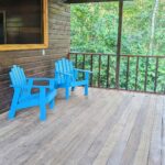 Two blue chairs on a porch with trees in the background.