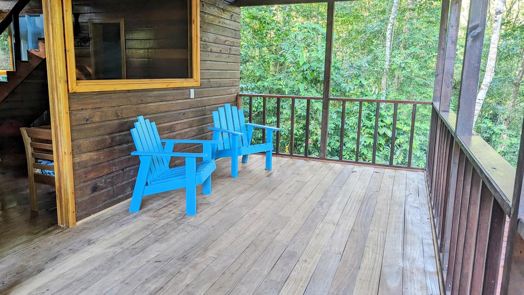 Two blue chairs on a porch with trees in the background.