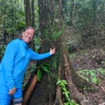 A man in blue shirt standing next to tree.