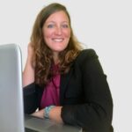 A woman sitting at her laptop smiling for the camera.