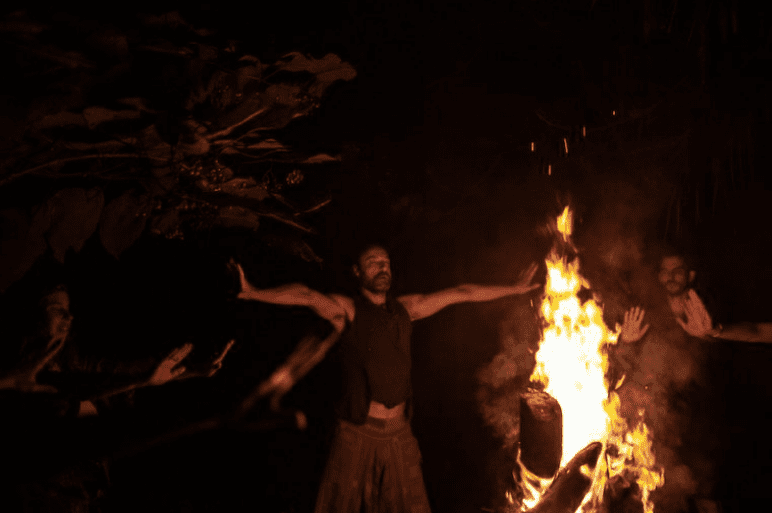 A man standing in front of fire at night.