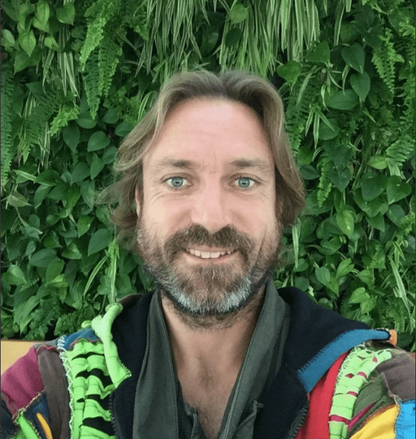 A man with long hair and beard wearing colorful clothing.